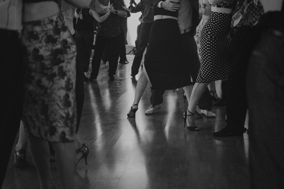 Adult guests on a dancefloor under coloured wash lighting with a DJ booth behind