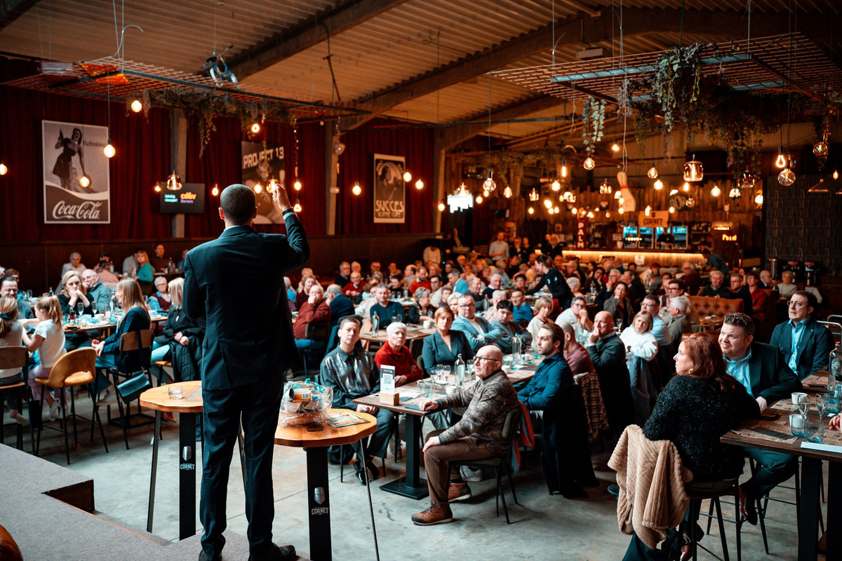 A busy mid-evening room with adults at activity tables and a host with a microphone